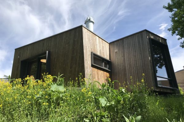 The exterior of the Outdoor Care Retreat. Its wooden structure stands tall against a summer blue sky; glass windows provide the cabin ample lighting. Photo credit: Maren Lindheim.