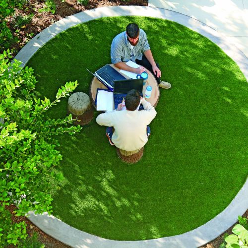 An aerial view of two people at a wooden table and stools working on their laptops together.