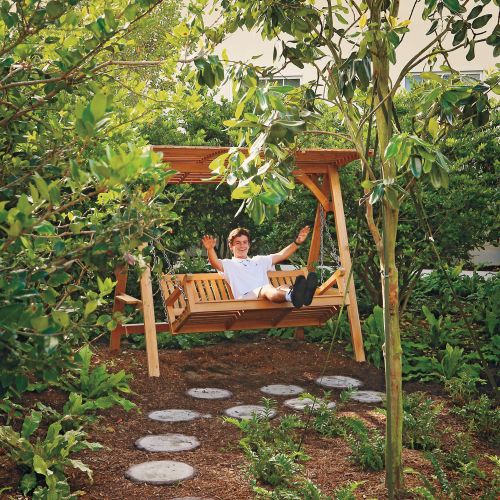 A young person sits on a swinging bench, smiling with their hands waving with joy in the air.