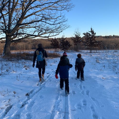 Under a clear blue sky, an adult and three children in cold-weather clothing leave tracks in the snow as they venture onto the prairie on a snowy day. The therapy groups are held outdoors in all kinds of weather and only canceled if weather conditions are dangerous.