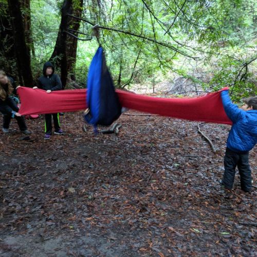 Outdoor Kids OT Playing the “bounce back” game, where one child in the swing sails into the “wall” of fabric held up by two other children.