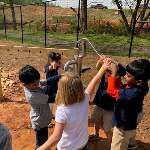 Three children team up to use a water pump as another child rinses his hands under the spout.