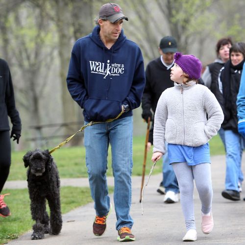 Founder Dr. David Sabgir walks his dog while chatting with a child at an event. In the background, several more people are walking in groups.