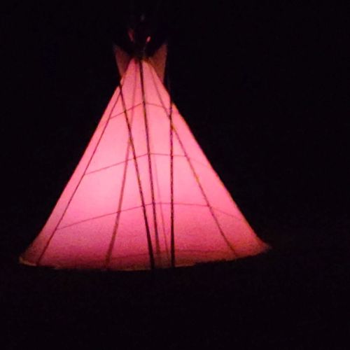 A tipi is lit with a red light from within. Outside it is pitch black.